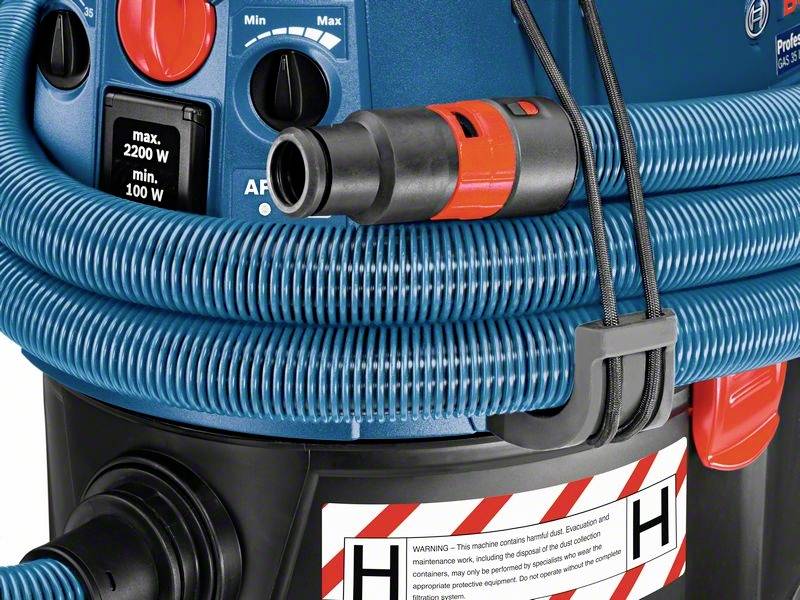 Industriële stofzuiger met rode netschakelaar, slang en waarschuwingssticker op blauwe behuizing toont maximaal vermogen van 2200 W.