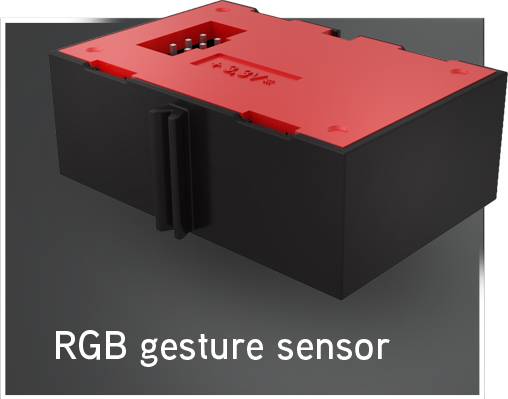 Een RGB-gebaarsensor in een zwarte en rode behuizing. Op de bovenzijde zijn kleine elektronische contactpunten zichtbaar.