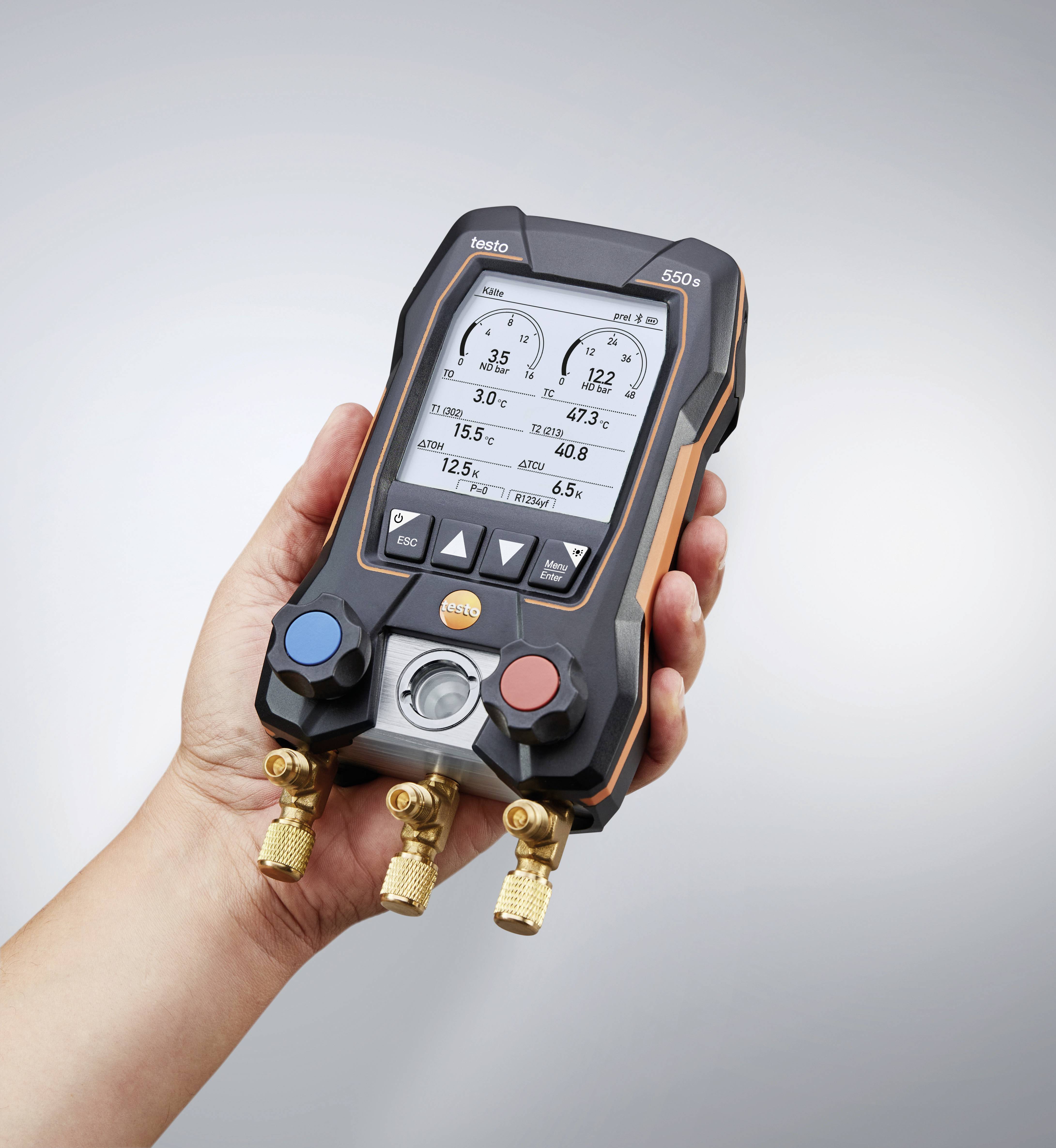 Een hand houdt een digitale manometer vast die druk en temperatuur op een display weergeeft. Het apparaat beschikt over rode en blauwe ventielen.
