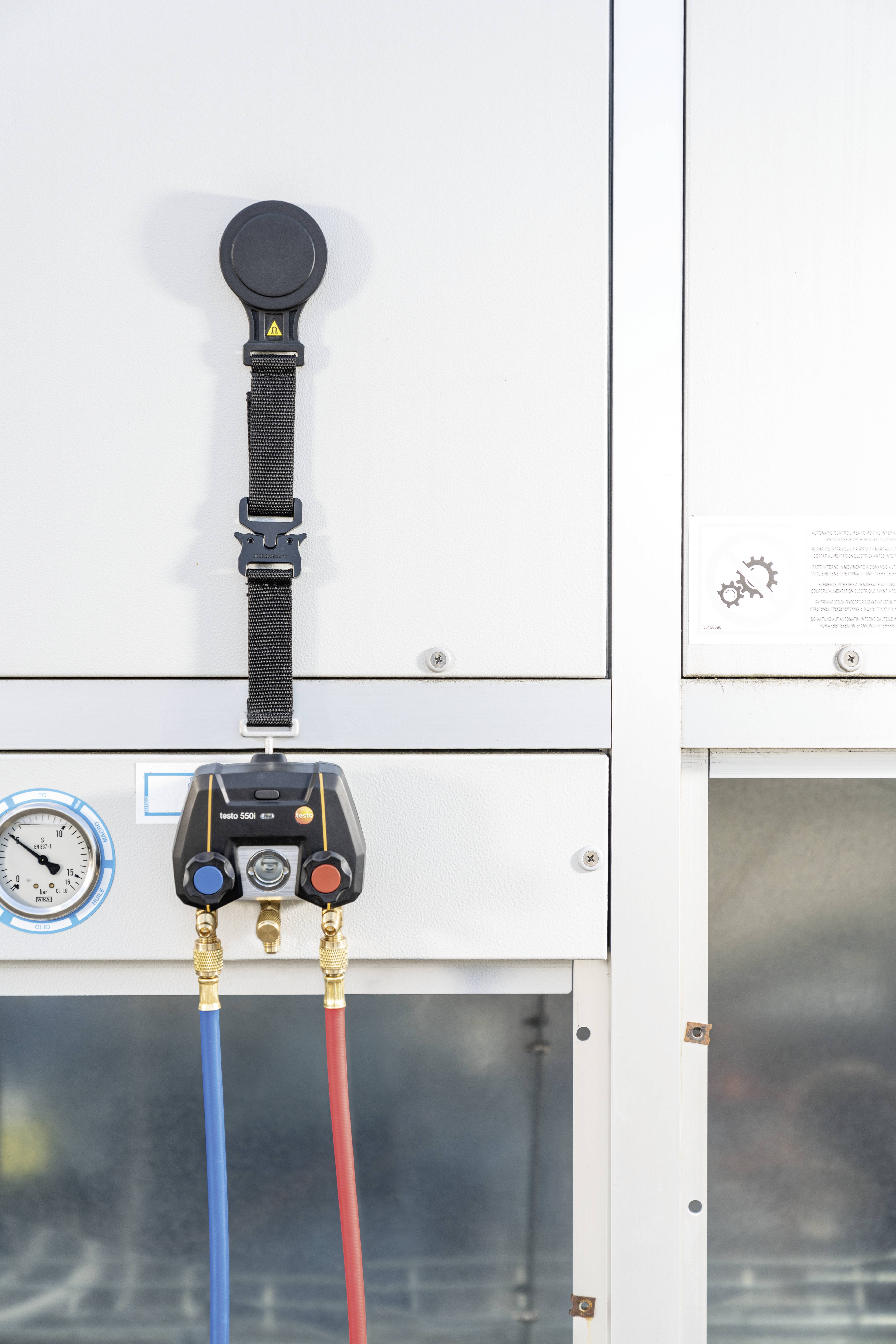 Een airconditioning met manometers voor drukmetingen. Twee slangen, één rood en één blauw, zijn verbonden. Apparaatonderhoud in uitvoering.