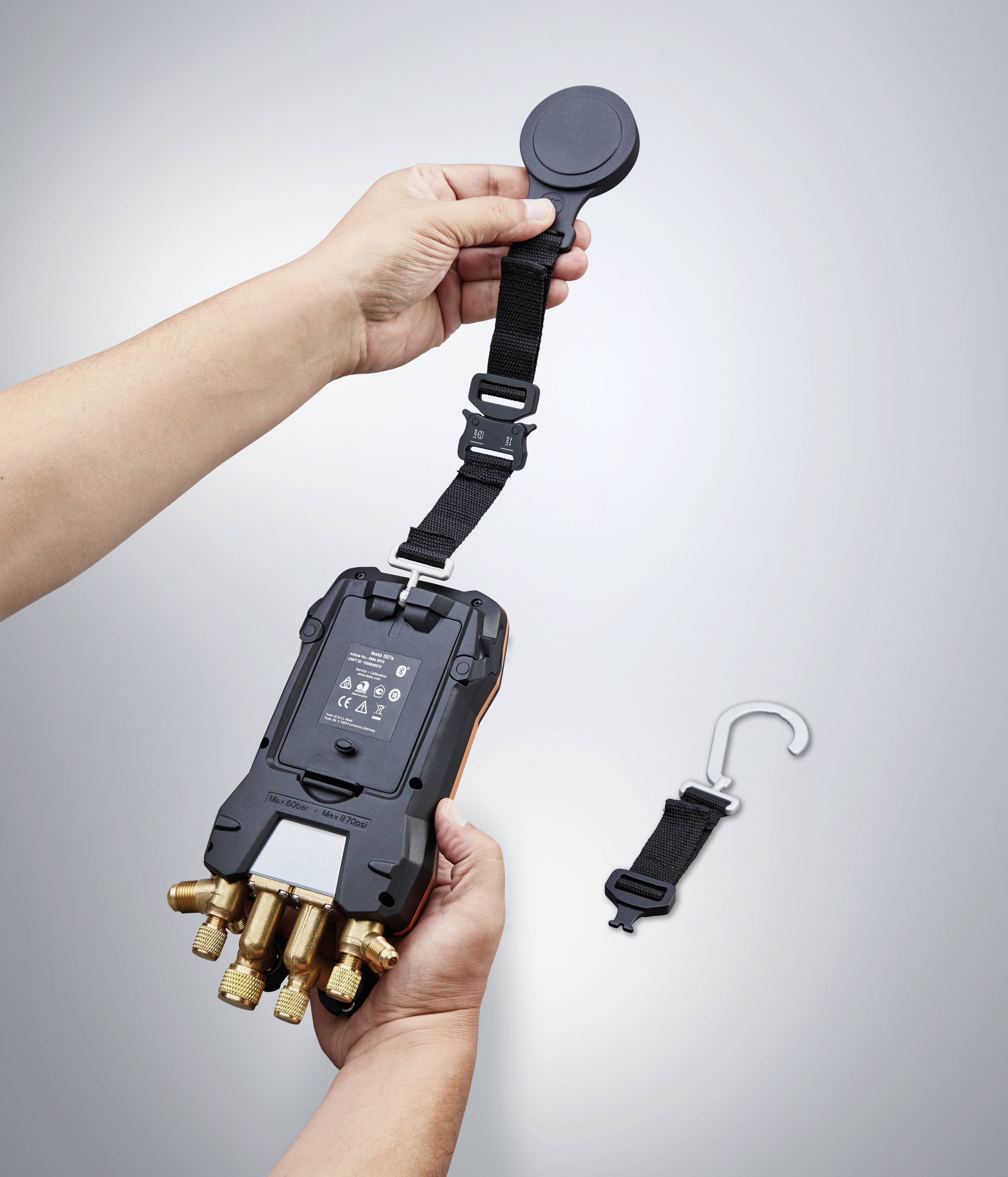 'Een persoon houdt een digitaal meetapparaat met meerdere aansluitingen vast, terwijl hij/zij een afneembare riem met een magneet bevestigt.'