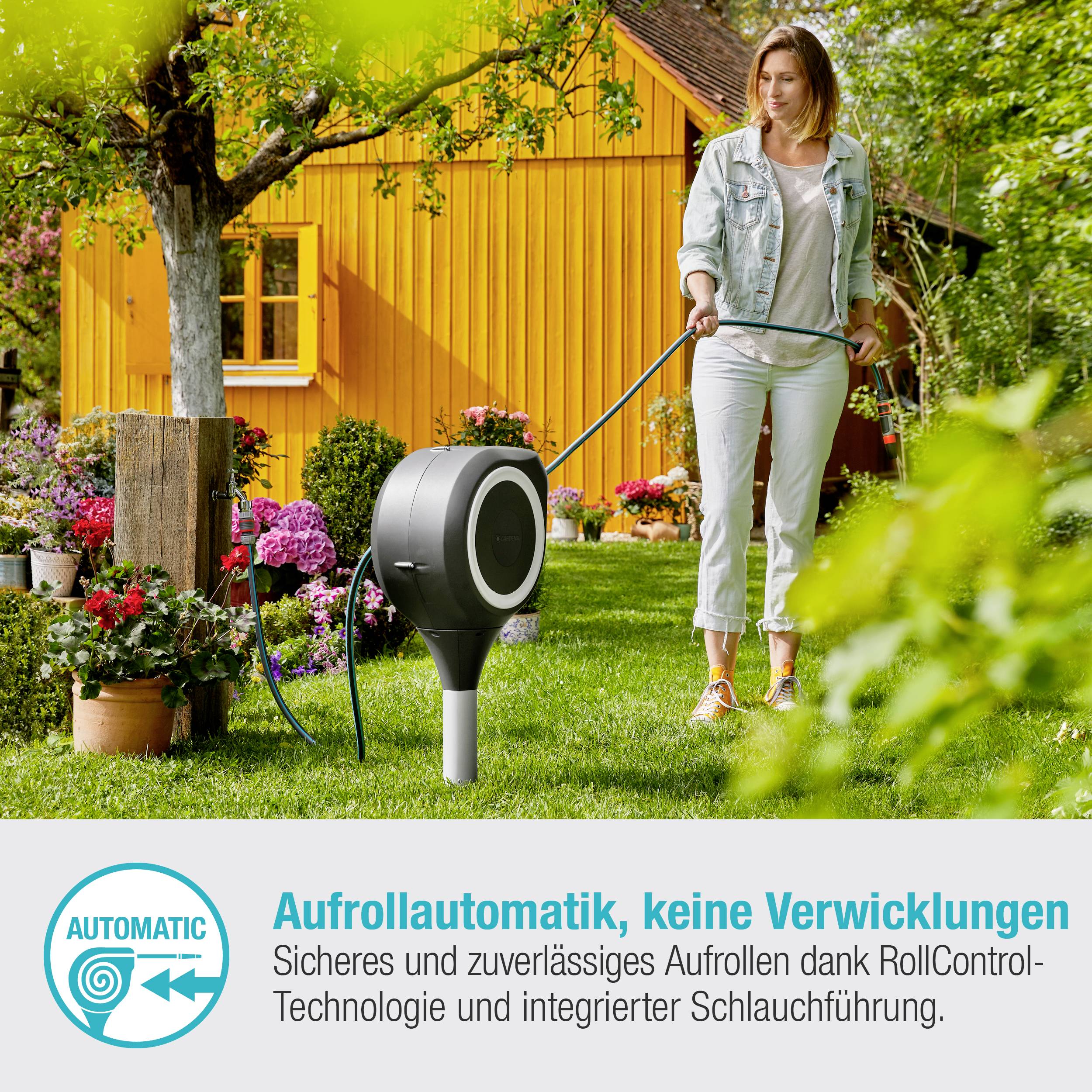 Een vrouw besproeit de tuin met een slang die wordt uitgetrokken van een automatische haspel. Op de achtergrond een geel huis.