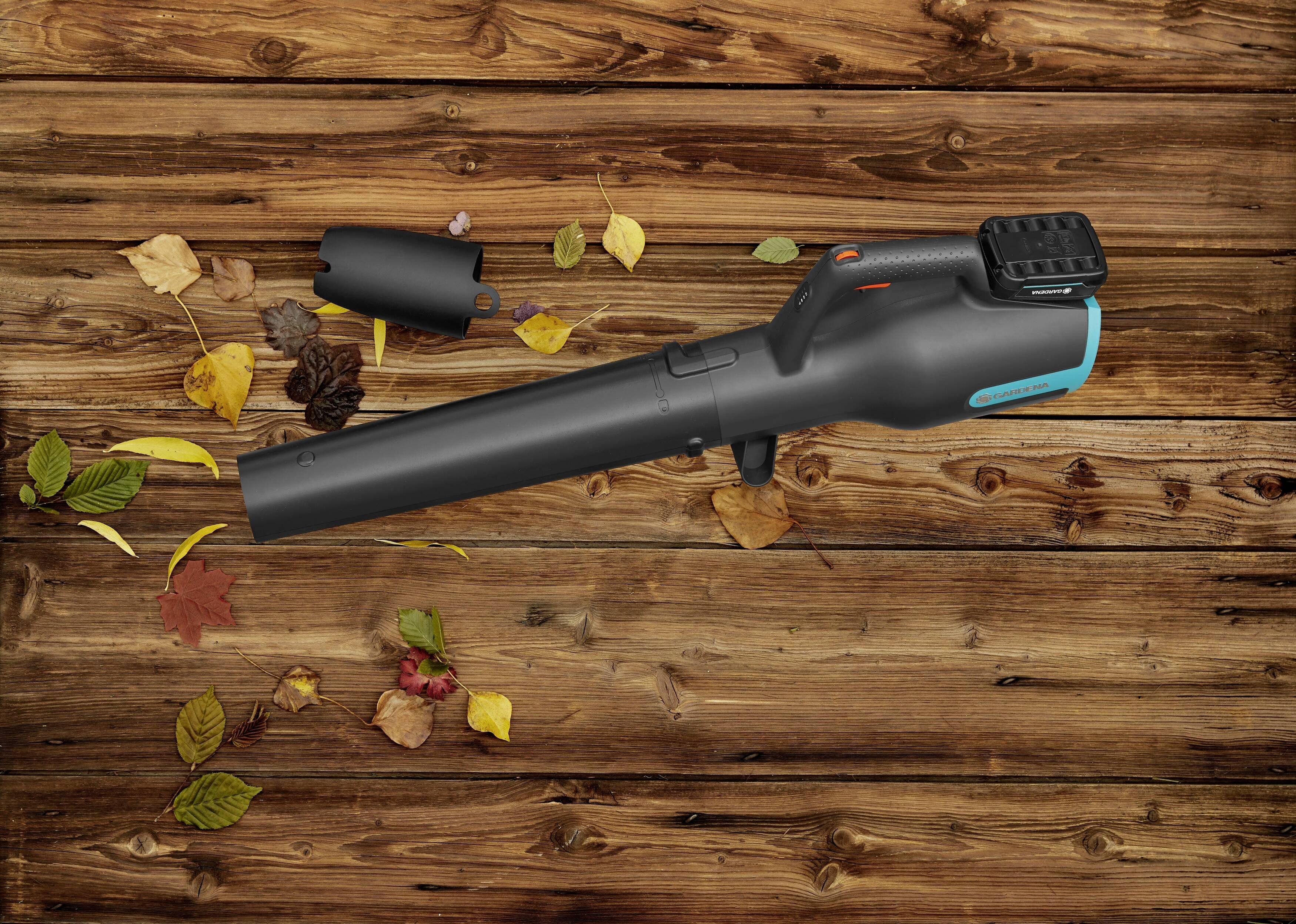 Bladblazer op een houten vloer met verspreid liggende herfstbladeren. Het apparaat is zwart met een turquoise accent.