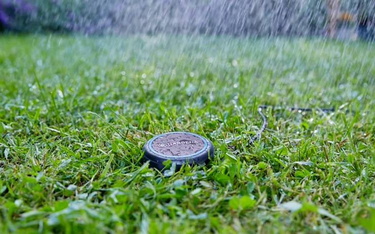 Een sprinkler besproeit een weelderig groen gazon, waarbij waterdruppels zichtbaar vallen, wat een frisse en levendige tuinscène creëert.
