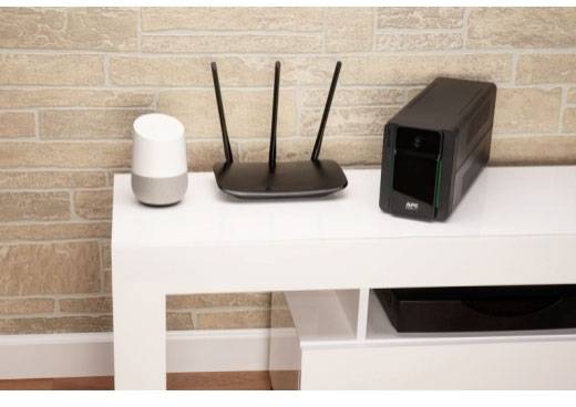 Een witte luidspreker, een zwarte router en een zwart NAS-apparaat op een witte tafel voor een gepatroneerde bakstenen muur.