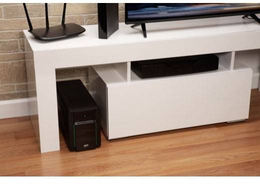 Een woonkamer-setup met een witte tv-kast. Op de vloer staat een zwarte pc-toren links naast de kast.