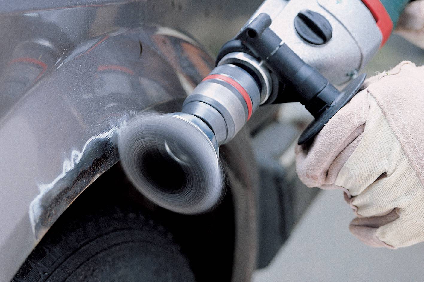 Een persoon polijst een autoportier met een elektrische polijstmachine om krassen te verwijderen. Handen dragen handschoenen.