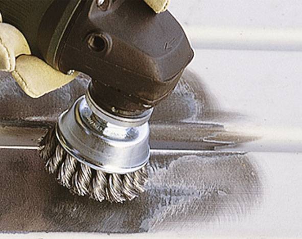 Een staalborstel wordt door een hand geleid, reinigt een metalen oppervlak. Het gebied wordt glad en glanzend.
