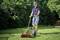 Een man maait het gras met een handmaaier in een zonnige tuin, omringd door groene struiken.