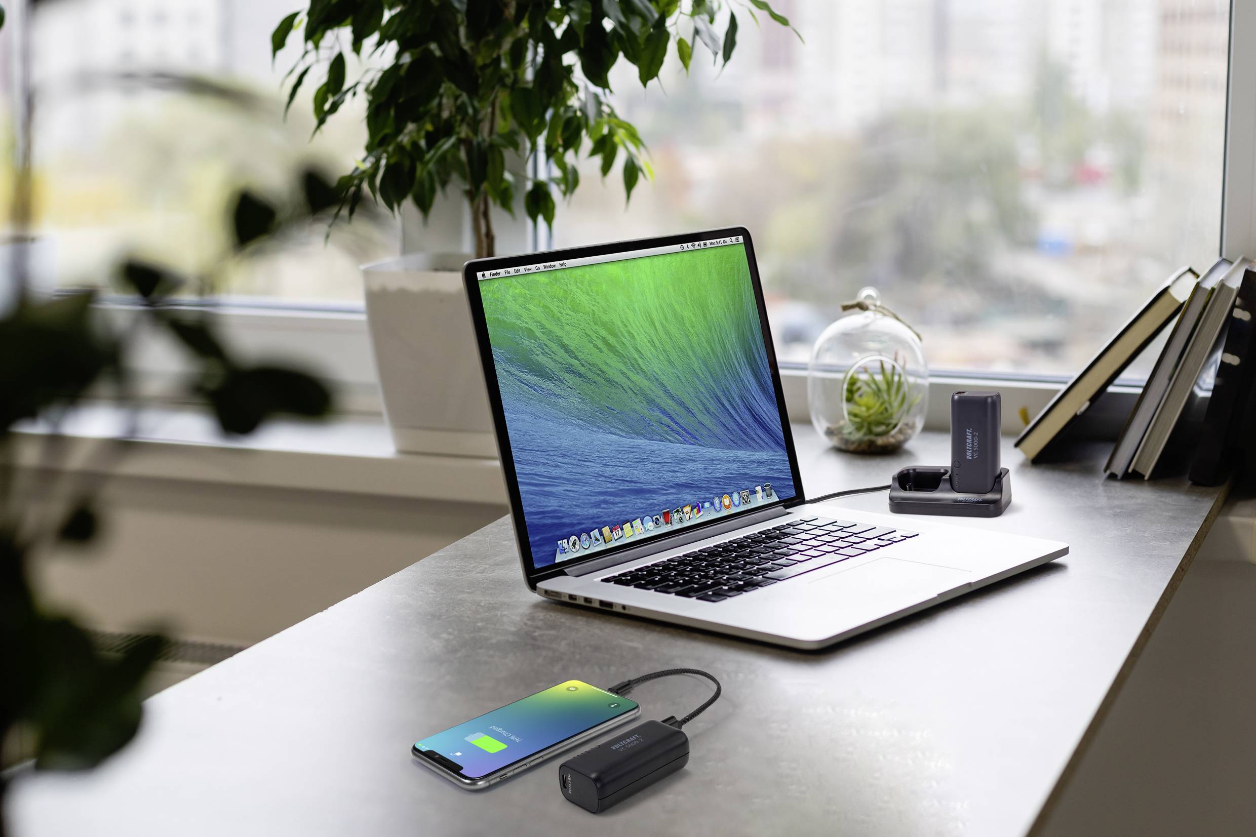 Een laptop op een tafel in een modern kantoor met uitzicht op de stad. Ernaast een smartphone en een powerbank.