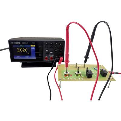Een digitaal meetapparaat meet elektronische componenten op een printplaat. Een scherm toont '2.026 µF'.