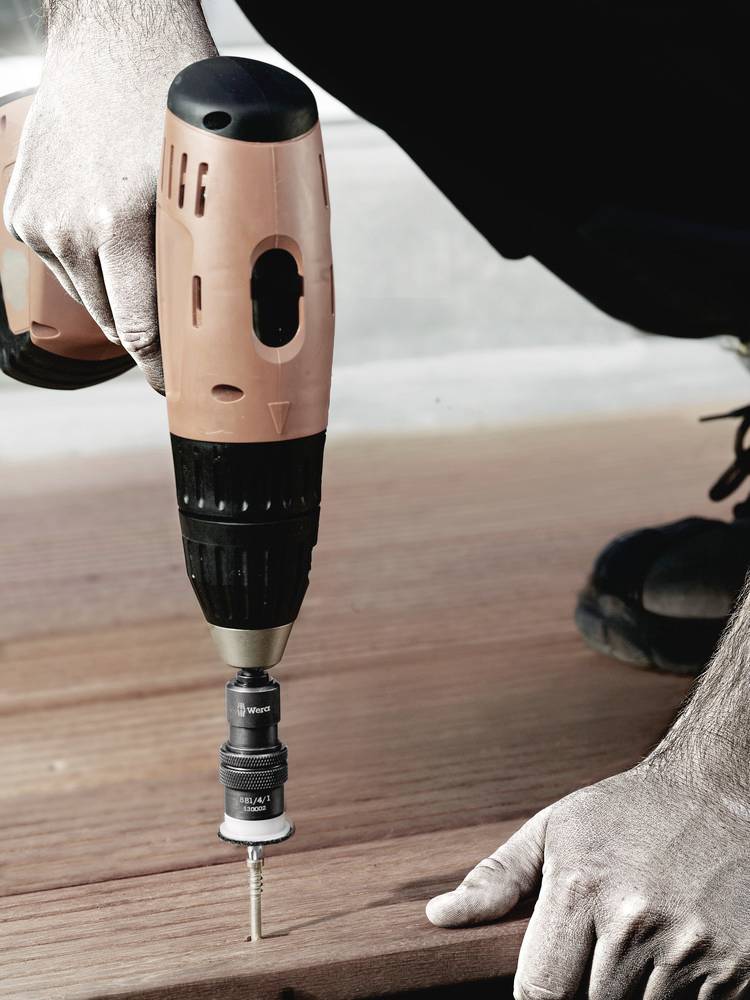 Een persoon gebruikt een accuschroevendraaier om een schroef in een houten plank te draaien. Handen houden het hout stabiel.