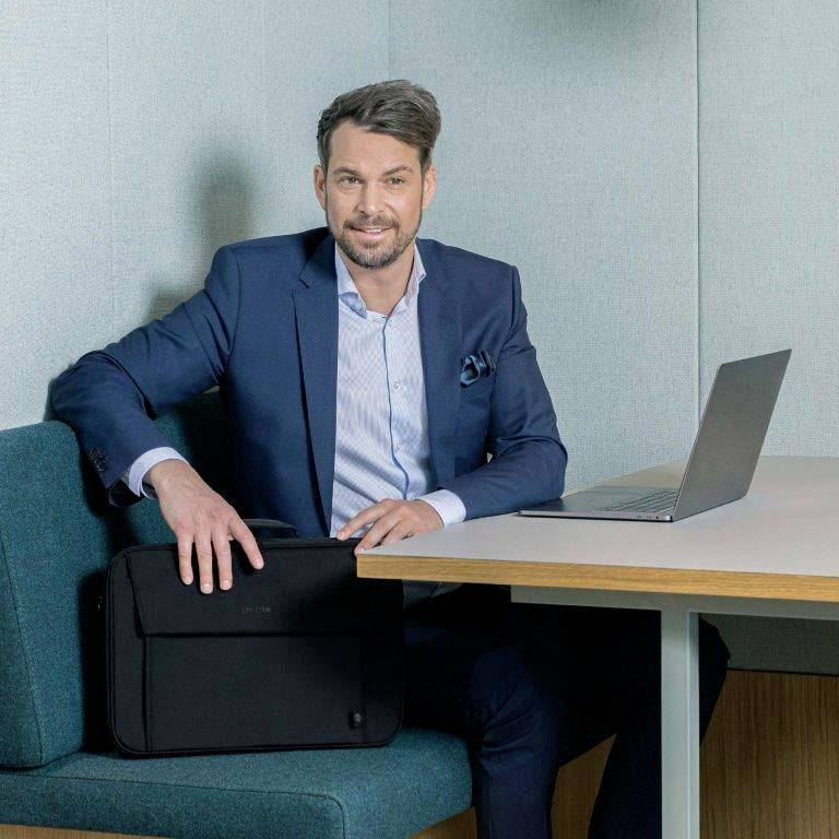 Een man in een pak zit in een moderne zithoek met een laptop op een houten tafel, klaar voor een vergadering.