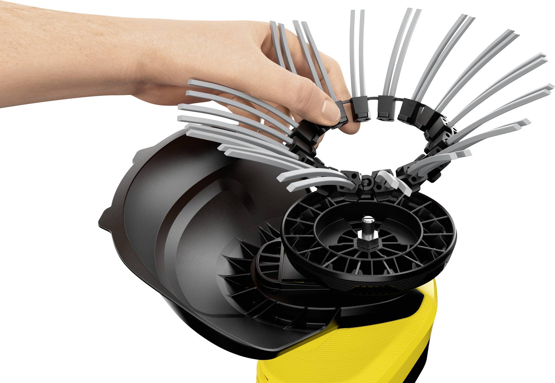 Een hand houdt een cilindrische reinigingsopzetstuk met flexibele grijze borstels en een zwarte basis, gemonteerd op een geel apparaat.