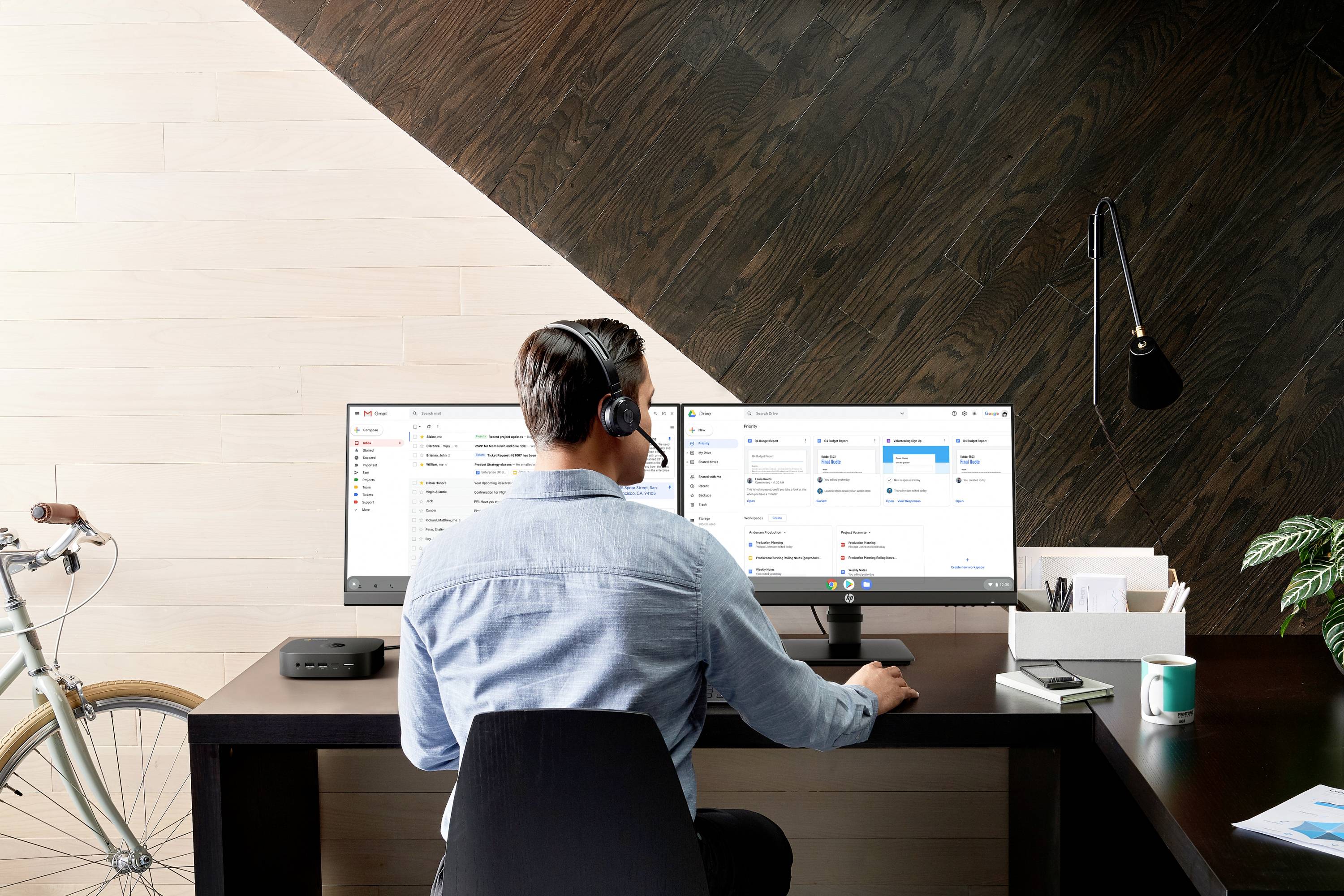 Een man werkt aan een bureau met twee monitoren, draagt een headset. Op de achtergrond staat een fiets tegen de muur.