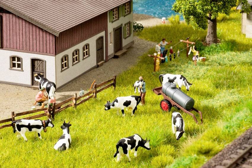 Koeien grazen op een weiland naast een boerderij; mensen werken op de achtergrond. Landelijke taferelen met groene velden en boerderijgebouwen.