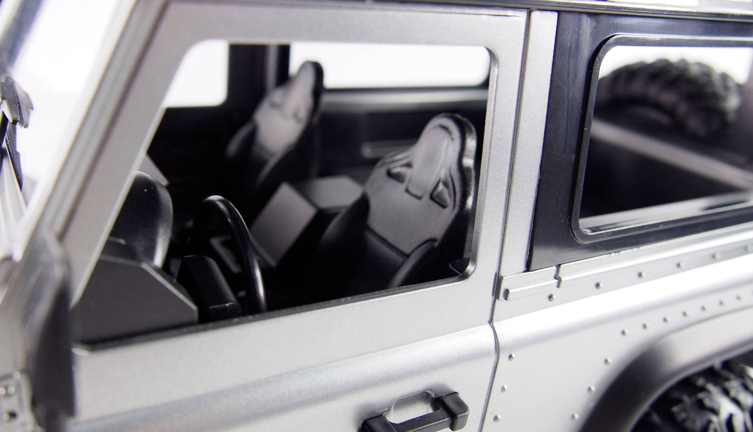 Close-up van het interieur van een terreinwagen, toont zwarte stoelen en een stuurwiel. Voor- en zijramen zijn zichtbaar.