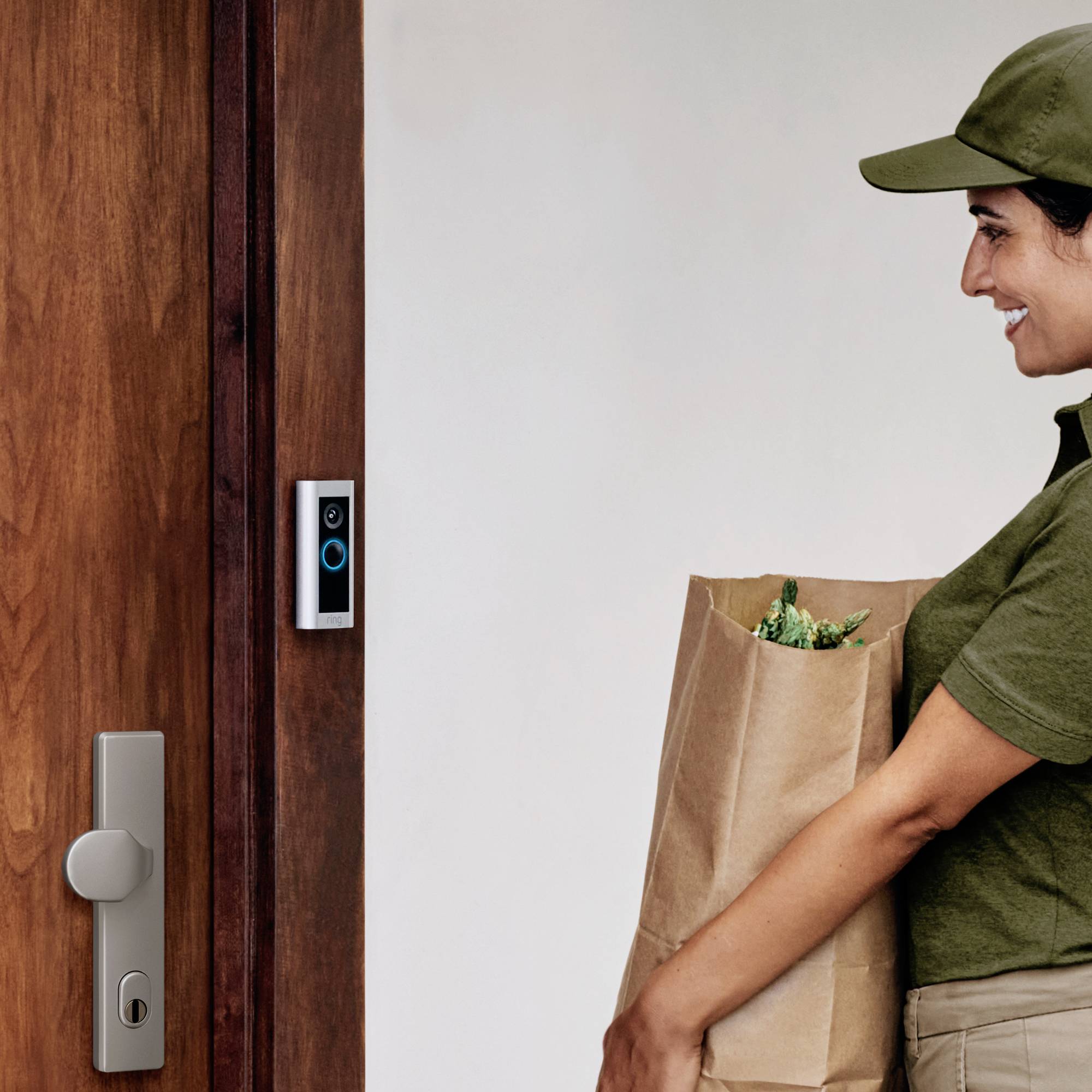 Een persoon in uniform staat voor een deur met een deurbel-camera en houdt een papieren zak vast, blijkbaar bezig met het uitvoeren van een bezorgdienst.