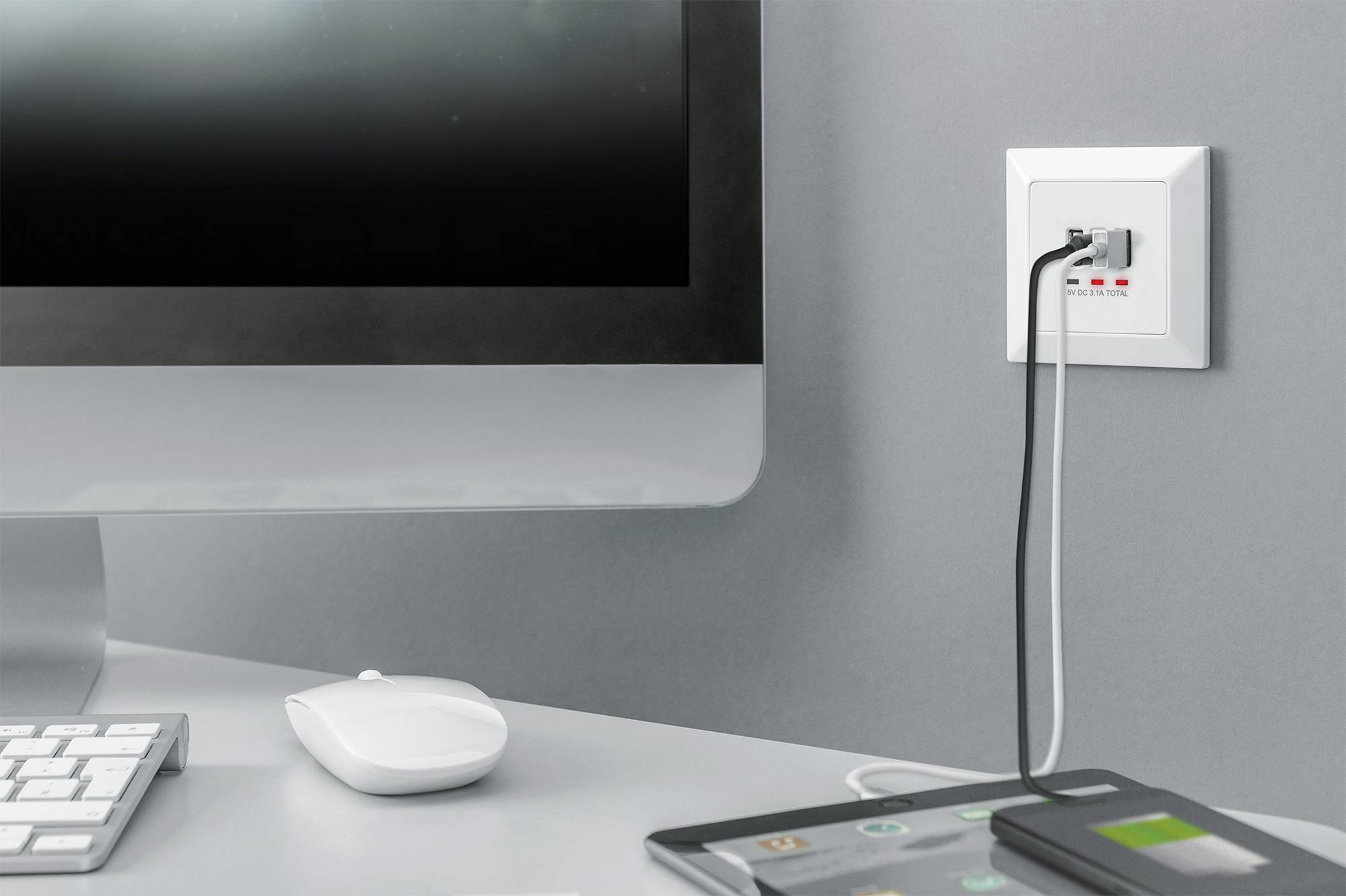 Een computerarbeidsplaats met monitor, muis en toetsenbord. Een kabel is in een stopcontact aan de muur gestoken.