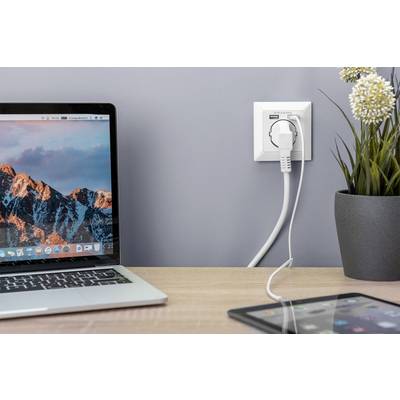 Een laptop op een tafel naast een stopcontact met een laadproces en een potplant. Een tablet ligt ernaast met een aangesloten kabel.