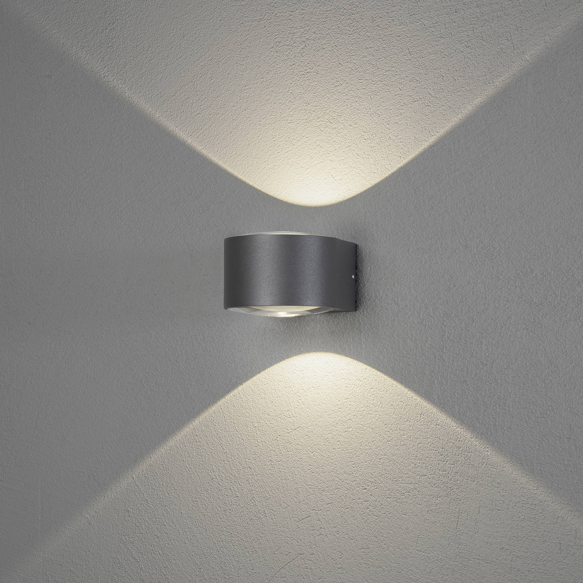 Wandlamp met een modern, metalen design straalt warm licht naar boven en beneden uit langs een crèmekleurige muur.