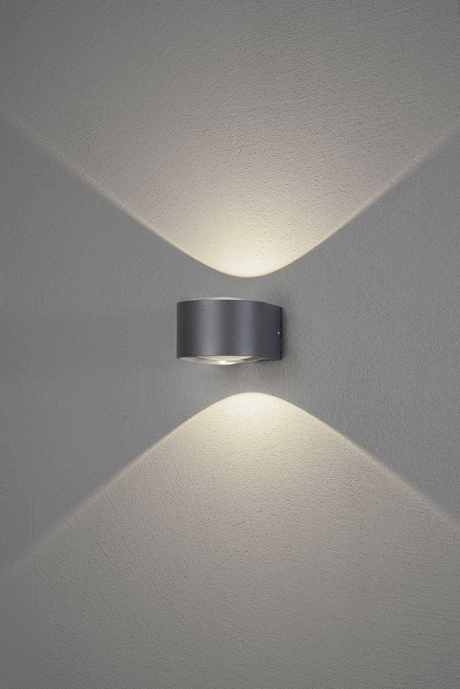 Wandlamp in modern design straalt licht naar boven en beneden uit, creëert een X-vormig patroon op de grijze muur.