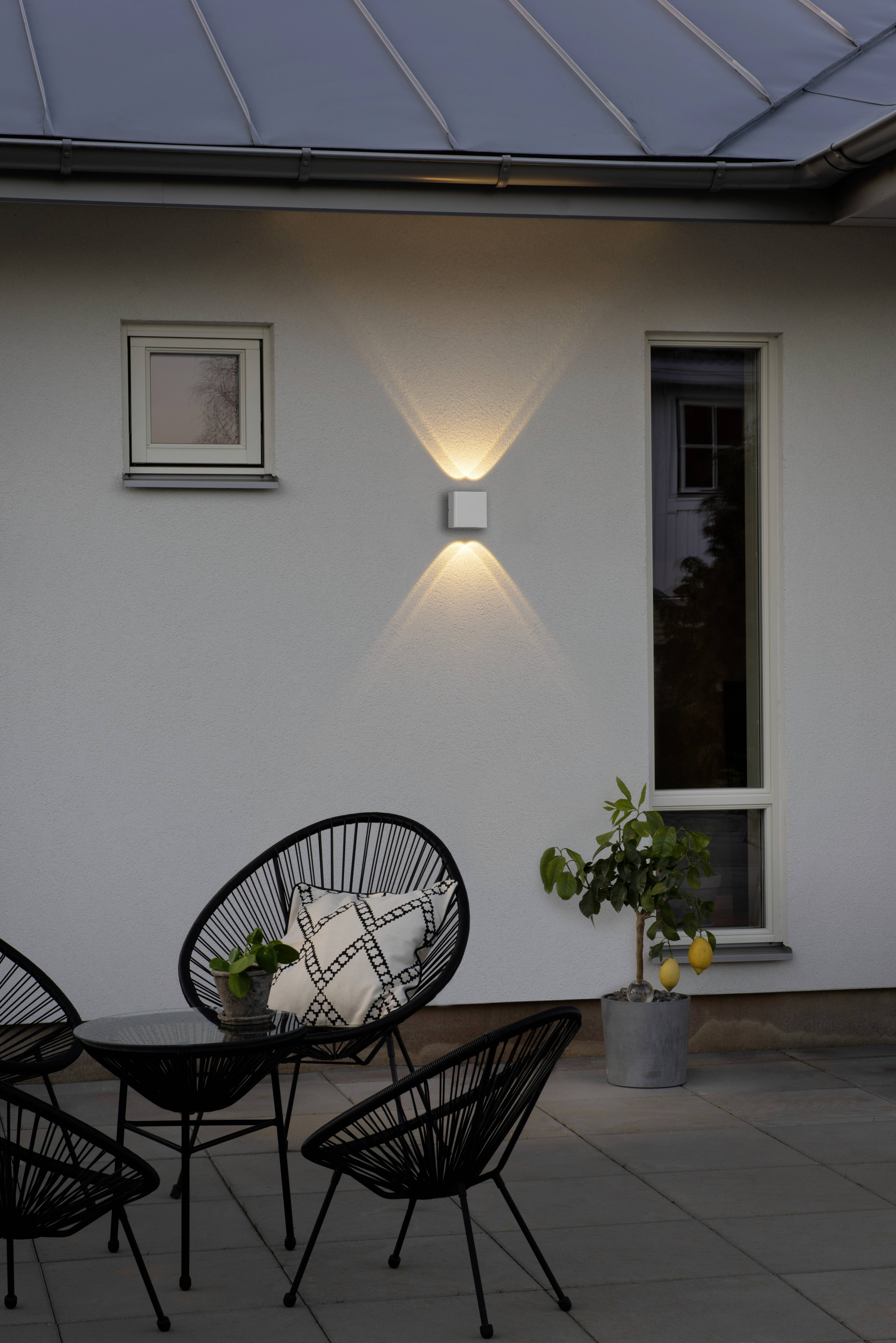 Terras met zwarte stoelen en een tafel, verlicht door een wandlamp. Een kleine citroenboom staat naast een raam.