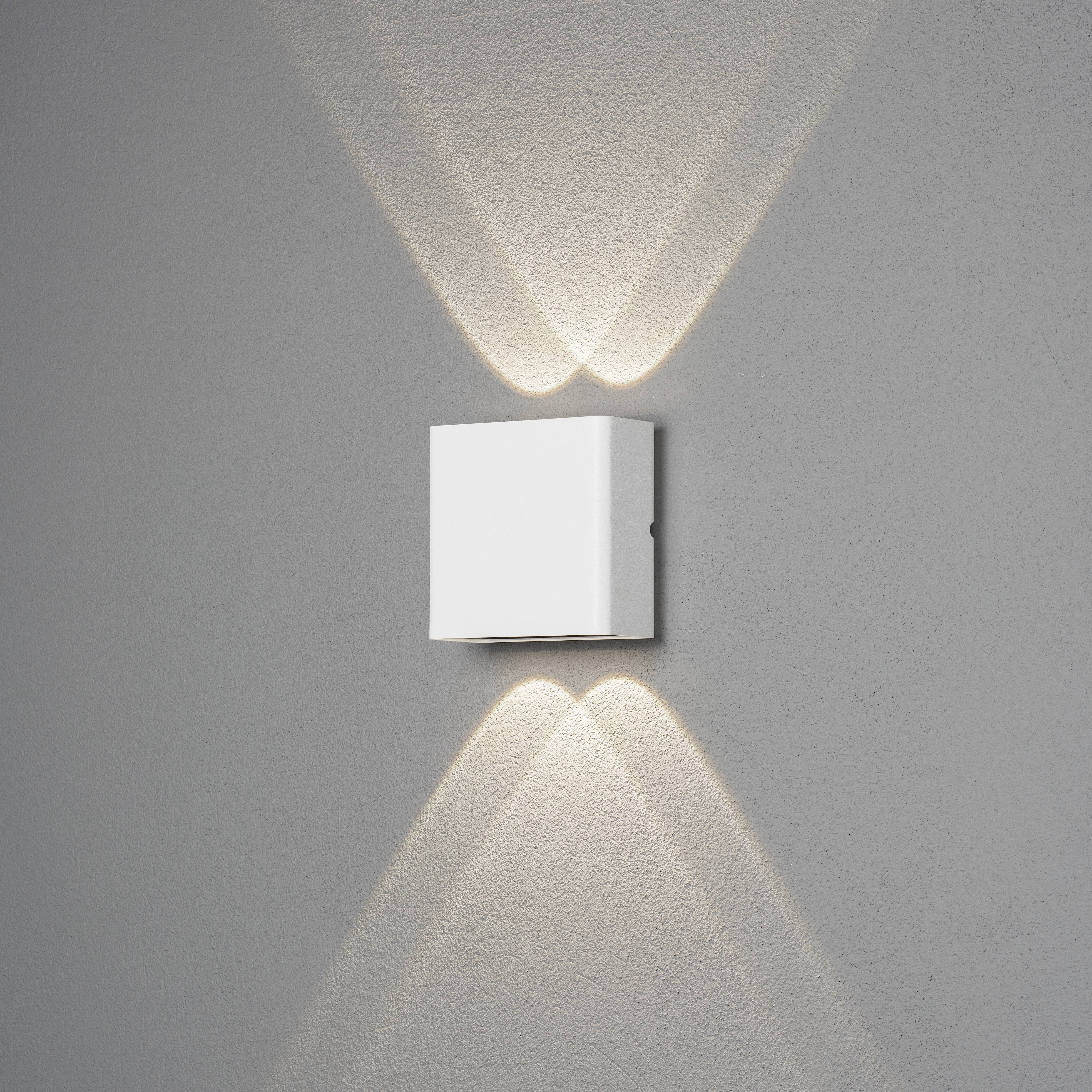 Een witte wandlamp werpt een symmetrisch lichtpatroon naar boven en beneden op een grijze muur.