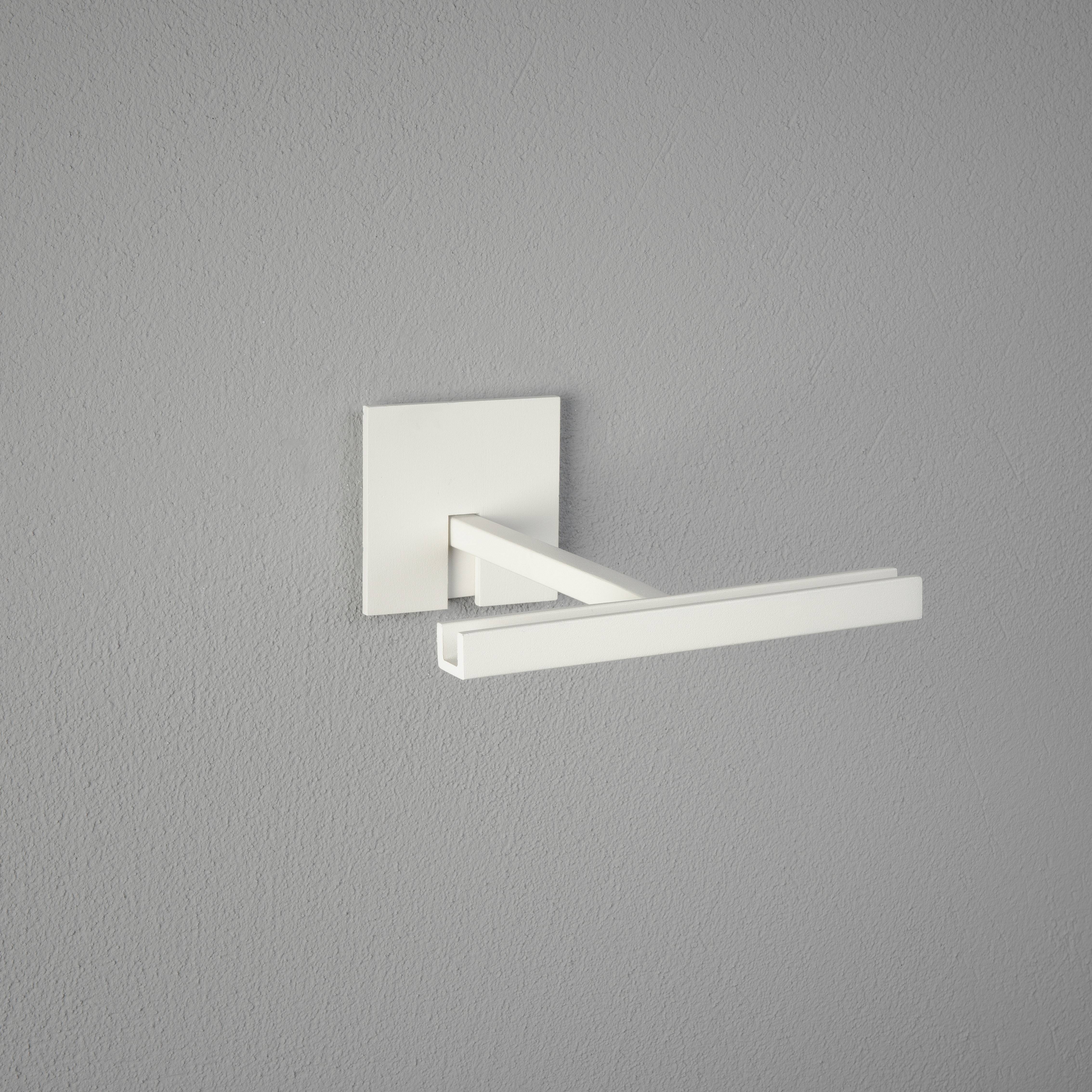 Witte, rechthoekige wandlamp op grijze muur. De lamp heeft een smal, horizontaal uitsteeksel en een vierkante voet.