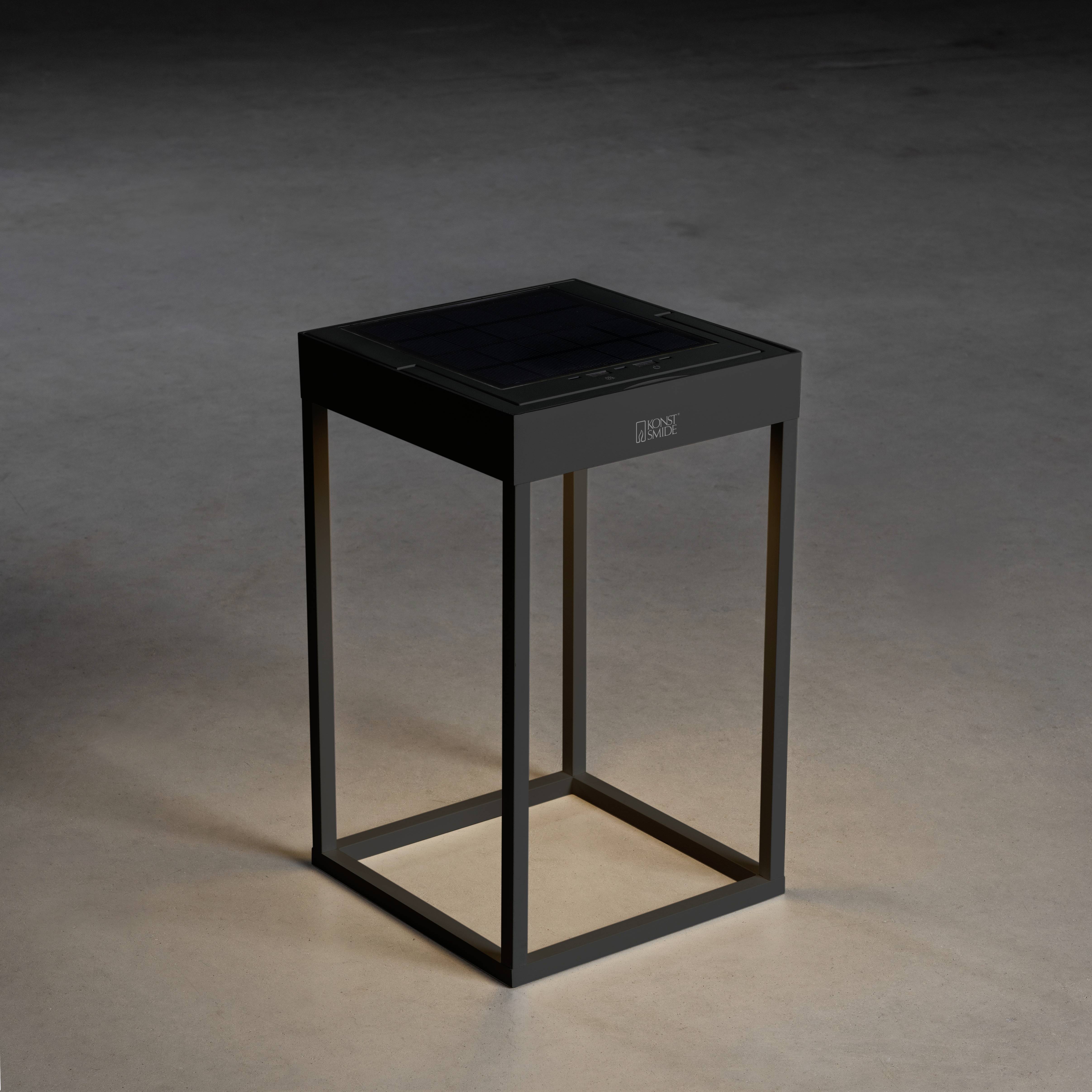 Een elegante, vierkante tafel met een donker frame staat op een grijze vloer. De tafel heeft een gladde, zwarte oppervlakte.