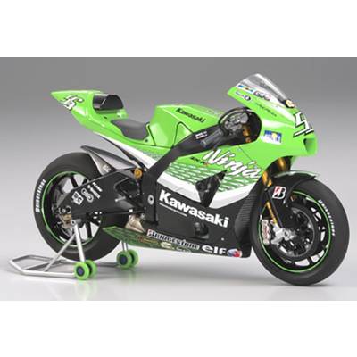 Een groene Kawasaki-racemotor staat op een standaard, klaar voor een race. Hij heeft reclamestickers en een racenummer op de kuip.