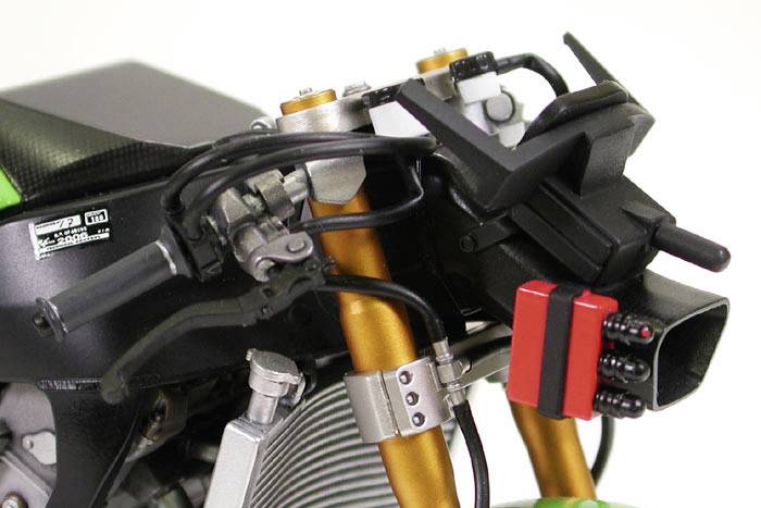 Close-up van een motorfiets met zichtbare gouden voorvorken, remsysteem en stuur, toont technische details van de voorwielophanging.