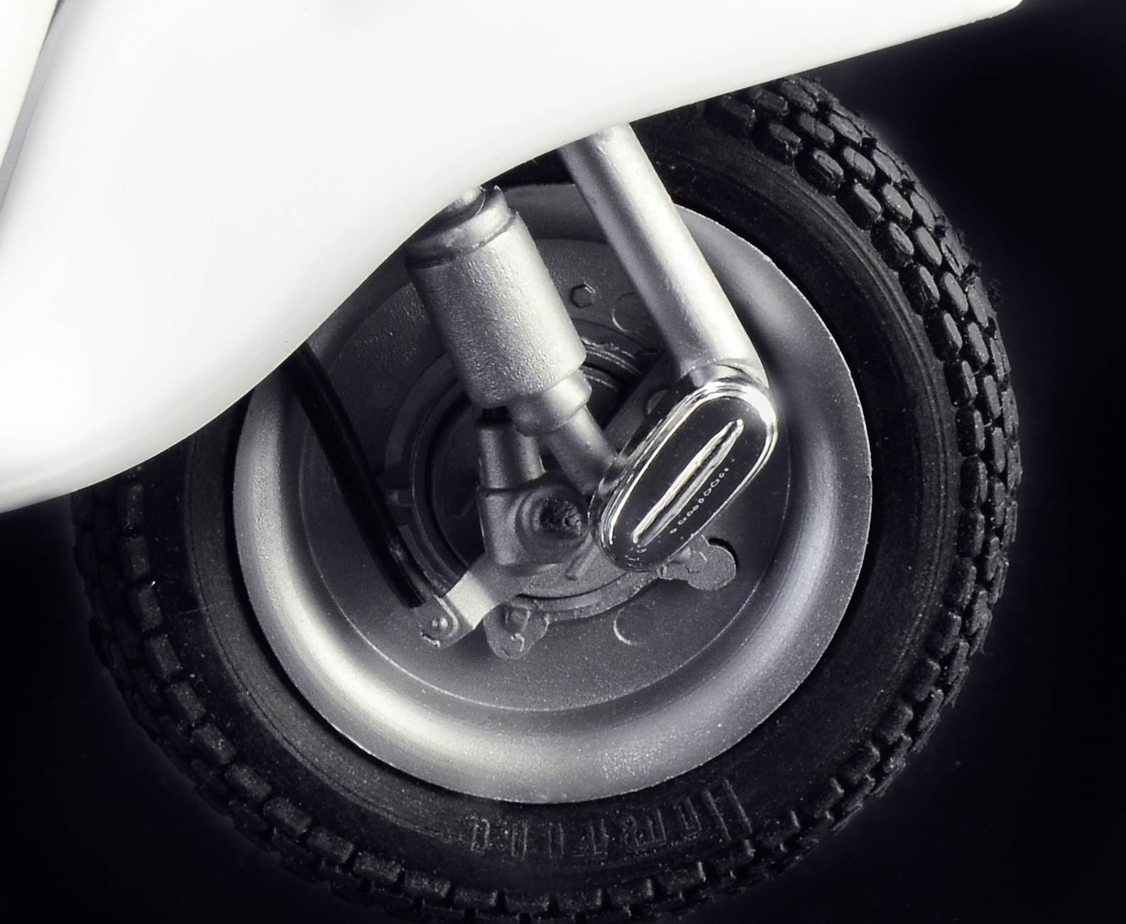 Close-up van een scooterband met zilveren velgen en zwarte banden. De schokdemper is zichtbaar, wat wijst op een voorwiel.