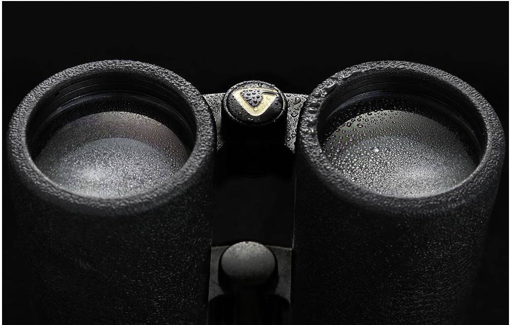 Verrekijker met waterdruppels op de lenzen, toont close-up van de vochtige oppervlakte tegen een donkere achtergrond.