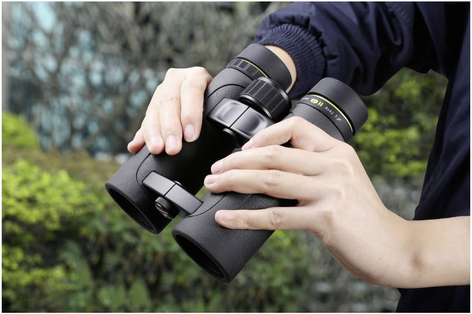 Een persoon houdt een verrekijker vast om landschappen te observeren. Op de achtergrond is onscherpe vegetatie te zien.