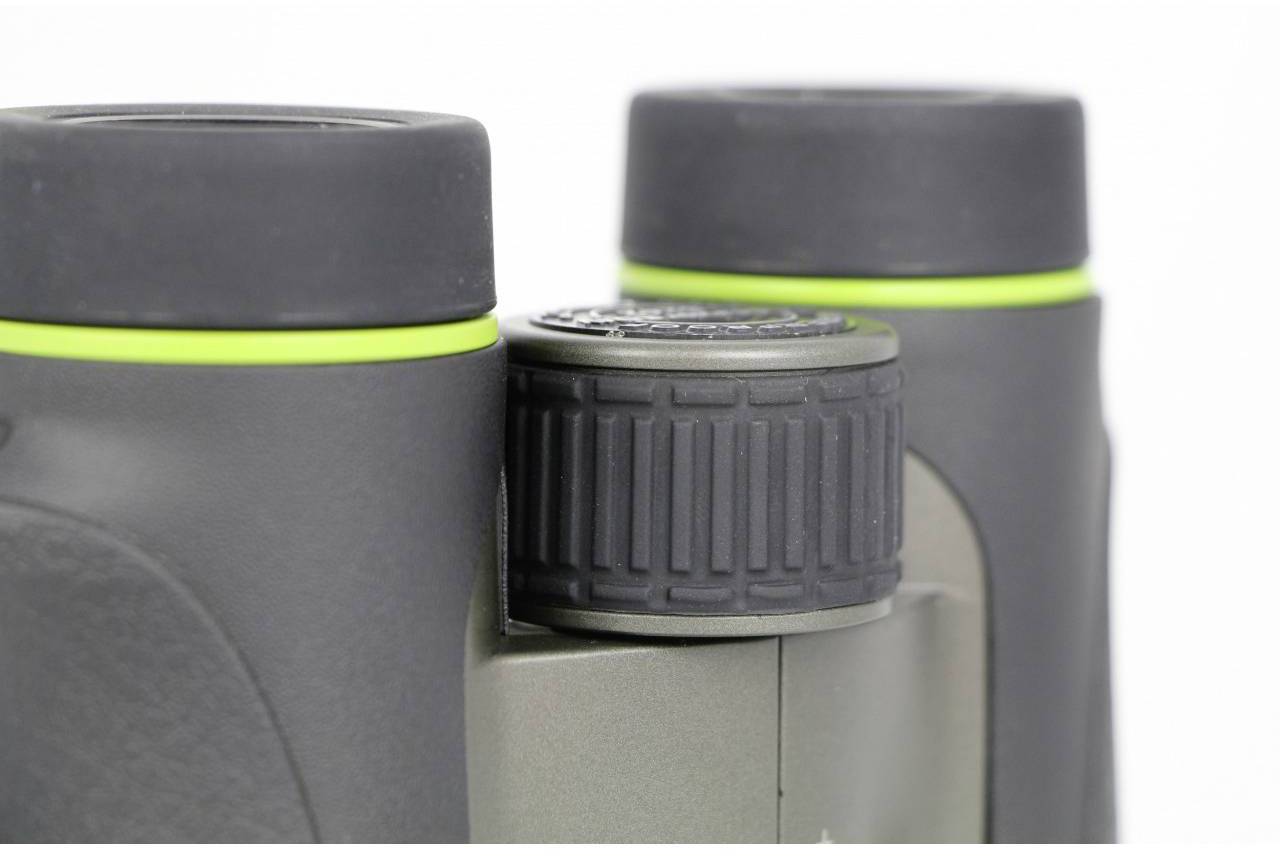 Close-up van een verrekijker met groen-zwarte kleurstelling. De focus ligt op het centrale stelwiel tussen de oculairs.