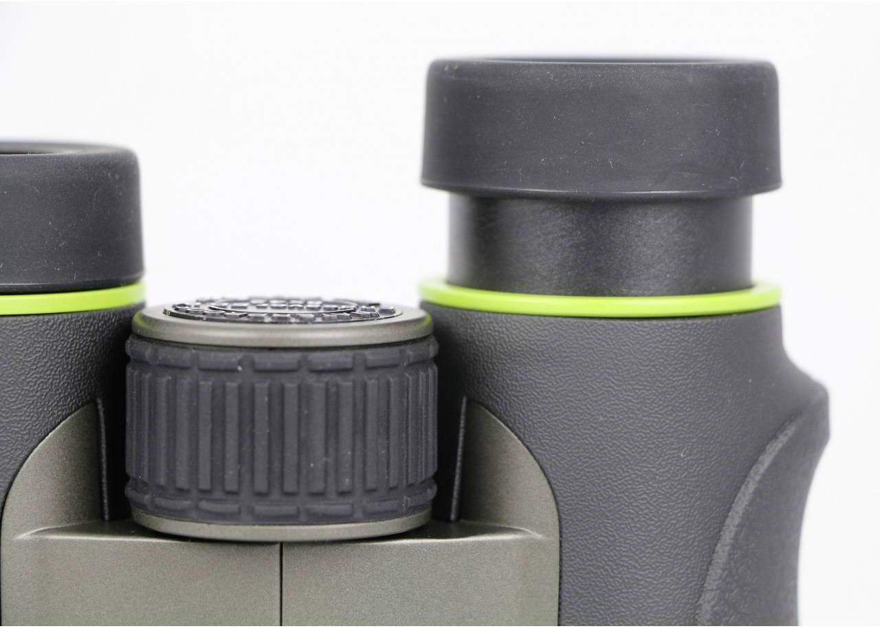 Een close-upfoto van een verrekijker met een zwarte en groene rand. Zichtbaar zijn focusmechanismen en oculairs.