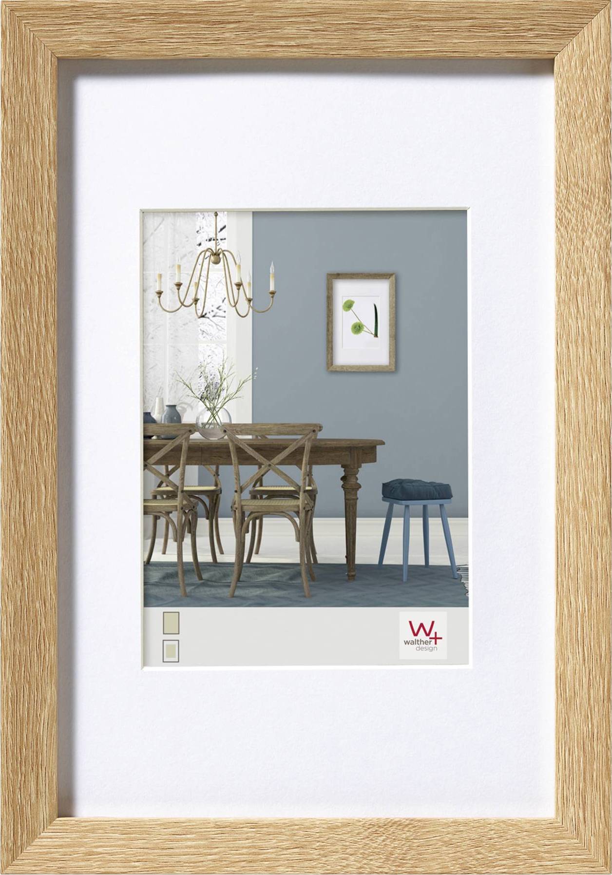 Een gedrukte afbeelding in een houten lijst toont een eetkamer met een tafel, stoelen, kroonluchter en een schilderij aan een blauwe muur.