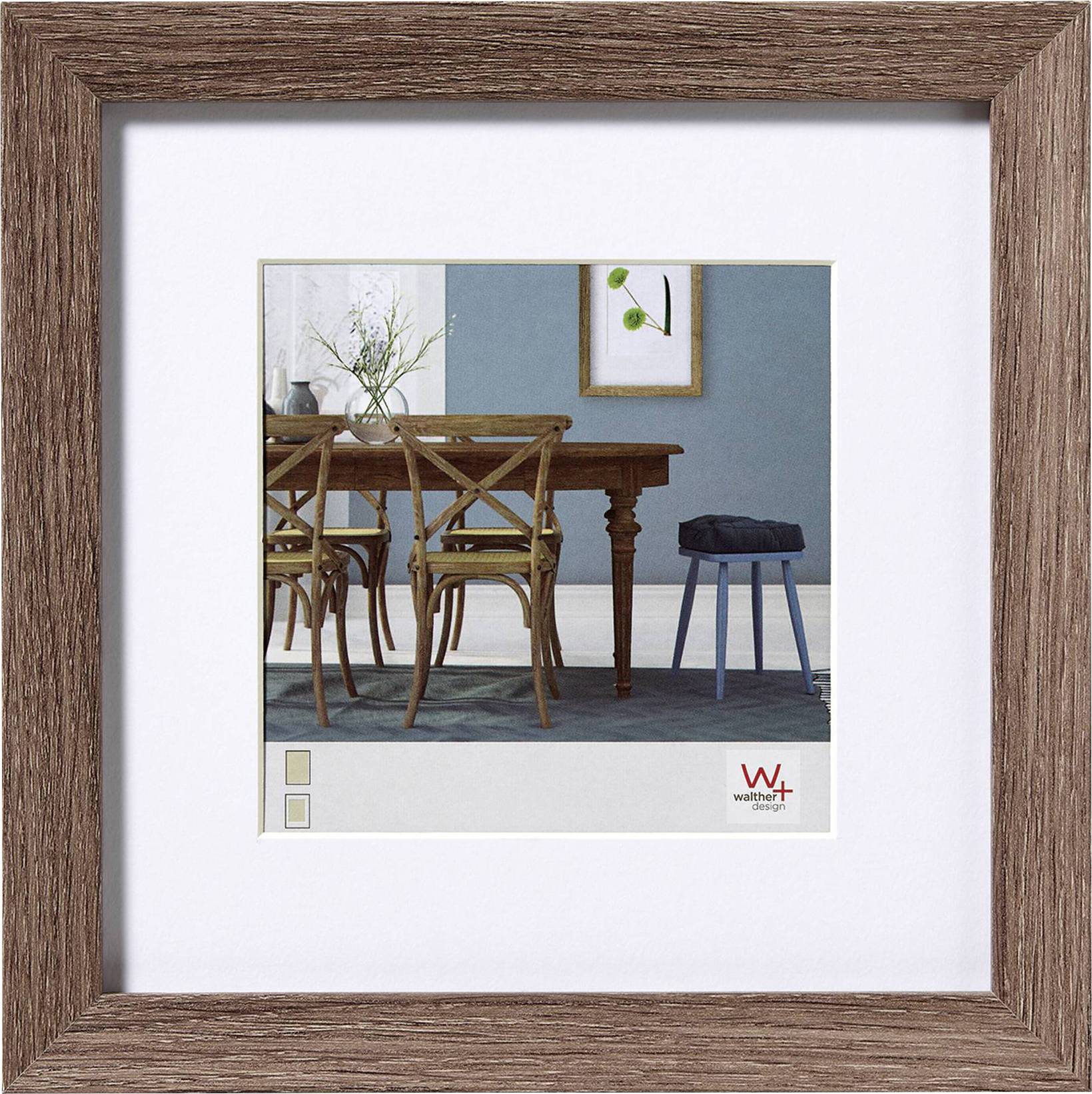 Een eetkamer met een houten tafel en vier houten stoelen. Aan de muur hangt een ingelijste foto. Rechts staat een kleine blauwe kruk met daarop een zwart kussen.
