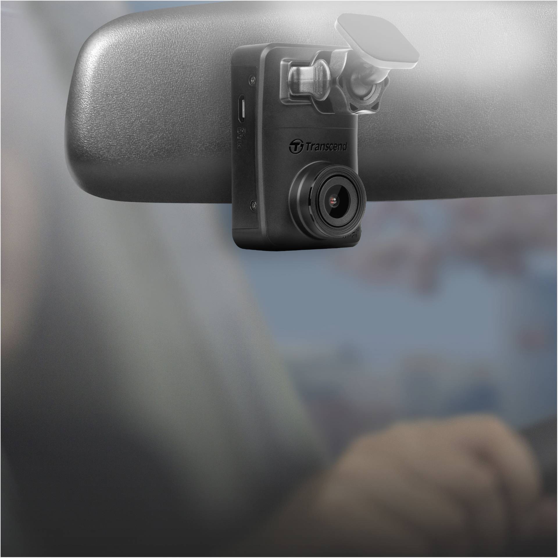 Een zwarte dashcam is bevestigd aan de achteruitkijkspiegel van een auto. Hij is gericht naar het interieur en documenteert de rit.