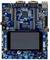 Een blauw microcontroller-ontwikkelingsbord met meerdere aansluitingen, chips en een LCD-scherm in het midden.