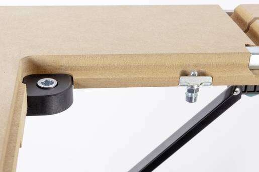 Een close-upfoto toont een houten plaat met metalen bevestigingen en een zwart kunststofwiel.