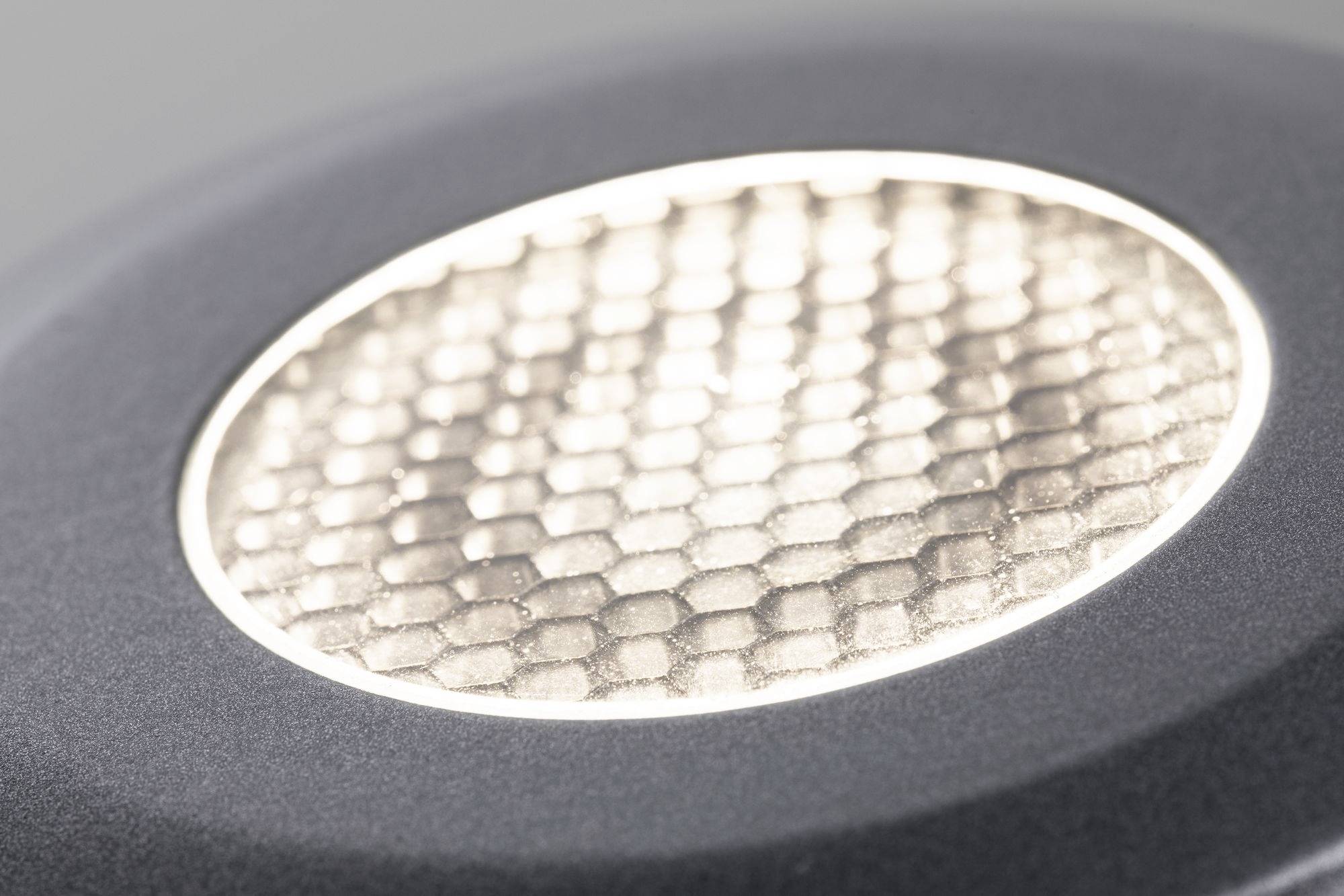 Close-up van een rond, honingraatvorming verlichtingselement dat is ingebed in een modern, grijs behuizing.
