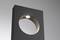 Een rechthoekig, donker object met een rond uitgesneden deel in het midden, bovenaan een ingebouwde verlichting. De achtergrond is lichtgrijs.
