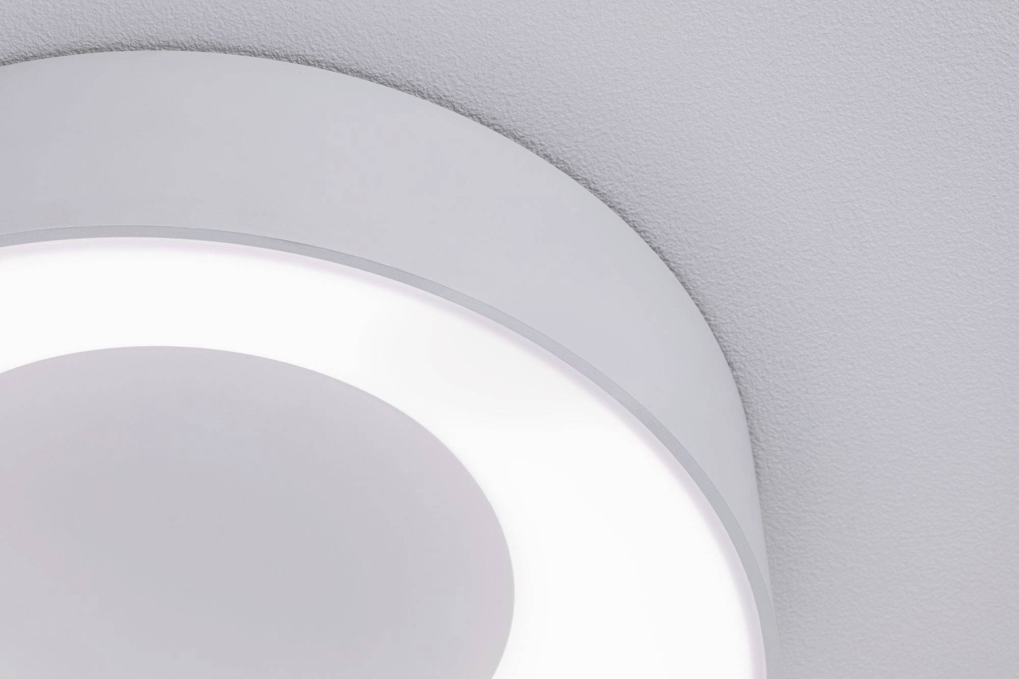 Een ronde, witte plafondlamp met een zacht lichtgevend effect aan een grijze plafond.