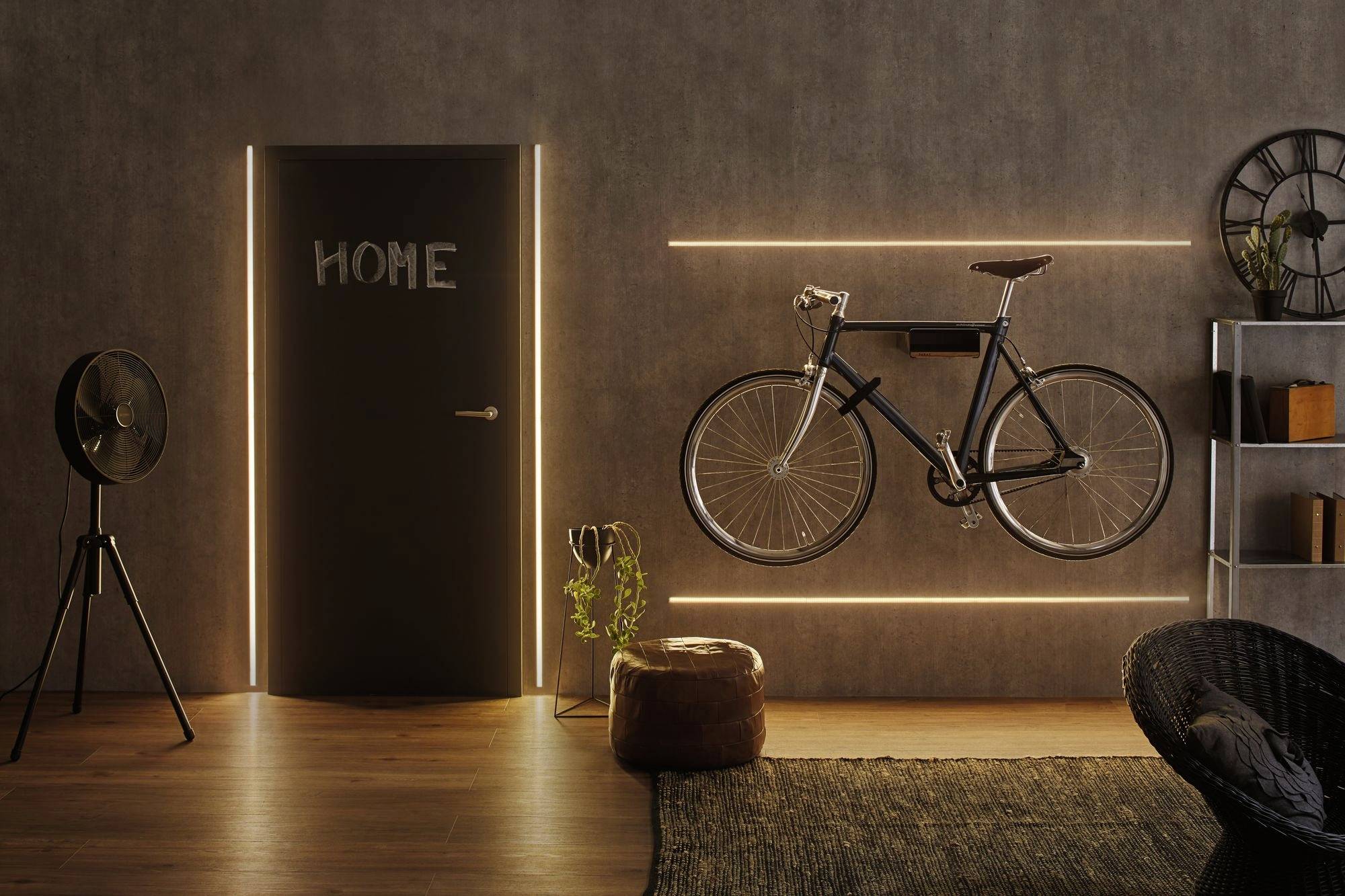 Sfeervolle interieuropname: Een stijlvol ingericht vertrek met een donkergrijze deur waarop 'HOME' staat. Een fiets hangt verlicht aan de muur.