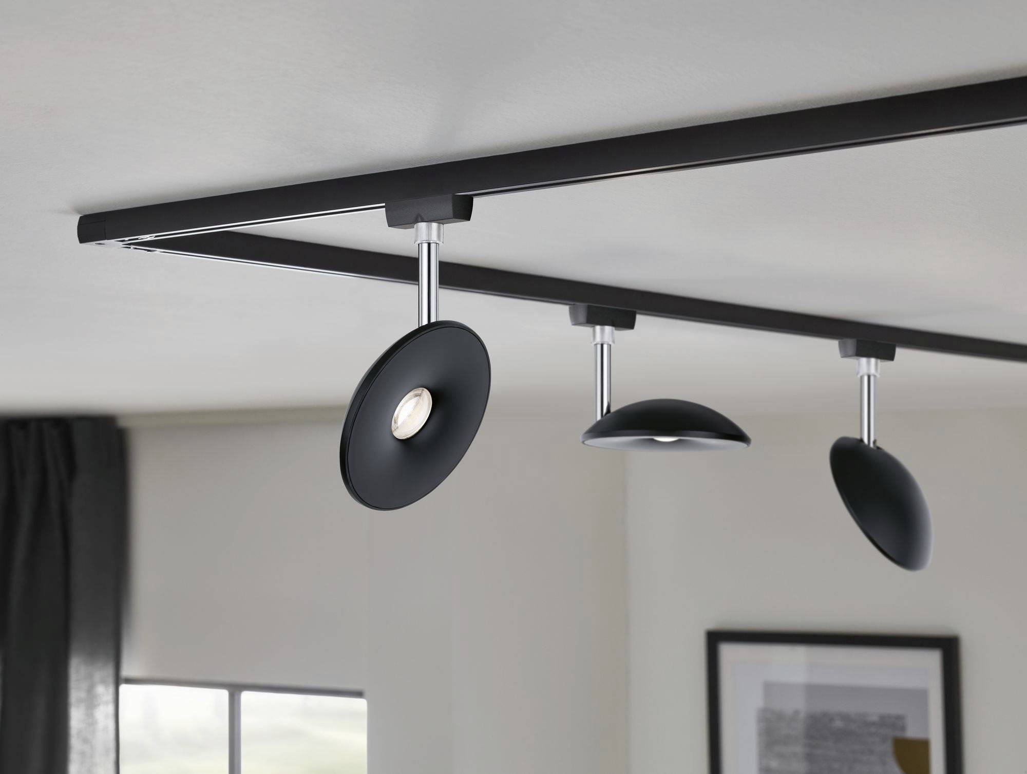 Plafondlamp met drie verstelbare, zwarte spots aan een metalen balk in een moderne woonomgeving.