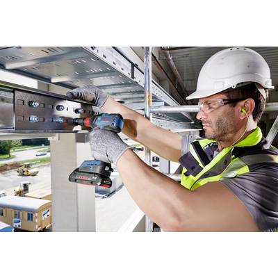 Een bouwvakker met een veiligheidshelm en handschoenen monteert metalen balken met een elektrische boormachine op een bouwterrein.