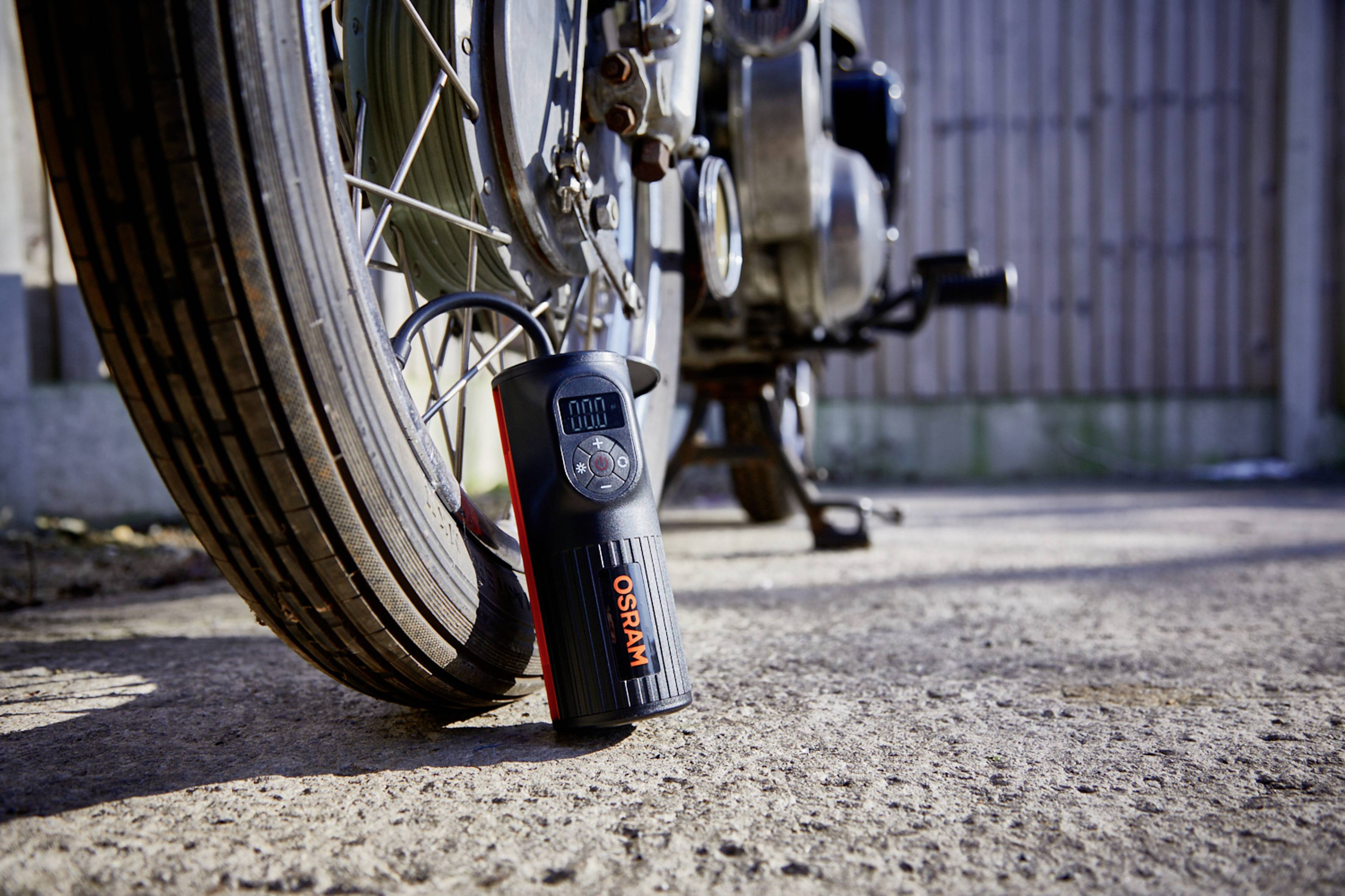 Een digitale bandenspanningsmeter ligt op de grond naast een motorband en toont de bandenspanning aan.