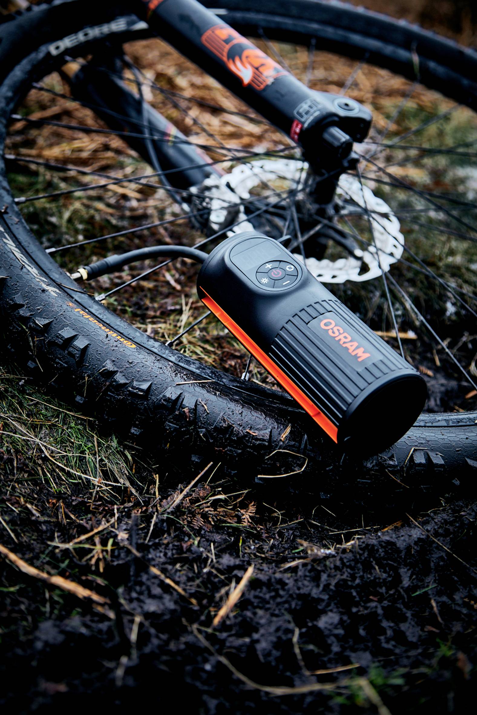 Fietsband oppompen met een luchtpomp in een vochtige omgeving. Een mountainbike ligt op de grond, de pomp is gemarkeerd met 'OSRAM'.
